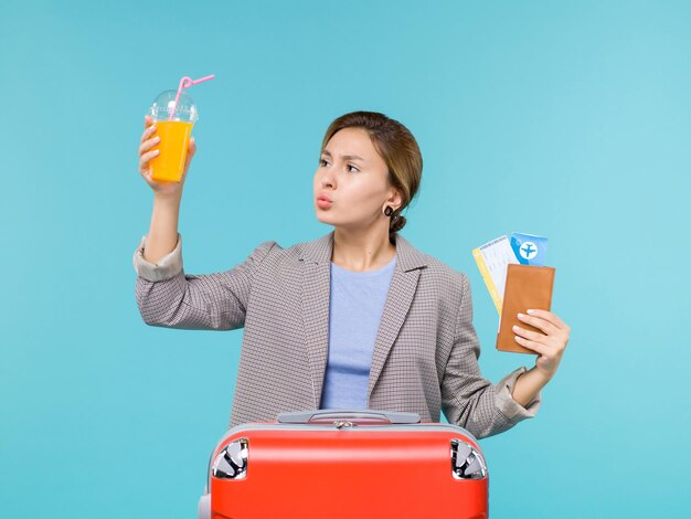 Front view female in vacation holding fresh juice and tickets on blue desk sea vacation plane voyage trip journey