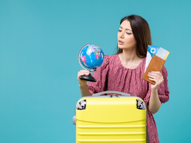 青い背景の海の休暇の女性の旅行の旅の夏に地球と飛行機のチケットを保持している休暇中の女性の正面図