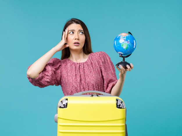 青い背景に小さな地球儀を保持している休暇中の女性の正面図海の旅女性旅行休暇夏