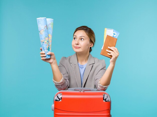 Вид спереди женщина в отпуске, держащая бумажник с картой и билеты на синем фоне, путешествие на самолете, морское путешествие, путешествие, отпуск