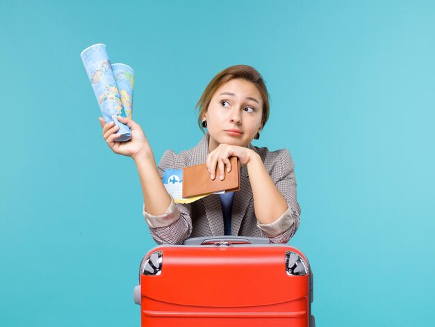 Вид спереди женщина в отпуске, держащая бумажник с картой и билеты на голубом фоне, путешествие на самолете, морское путешествие, путешествие, отпуск
