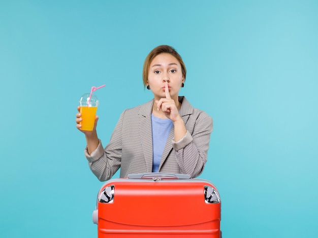Вид спереди женщина в отпуске с ее красной сумкой, держащей свежий сок на синем фоне, море, отпуск, самолет, путешествие, путешествие, путешествие