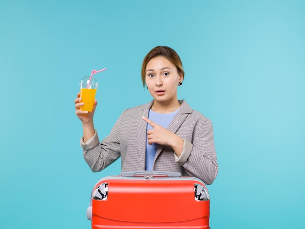 青い背景の休暇の飛行機の航海海の旅の旅でフレッシュジュースを保持している彼女の赤いバッグと休暇中の正面図