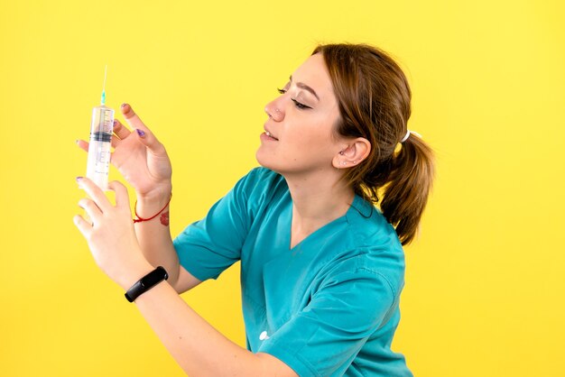 黄色の壁に注射を保持している女性獣医の正面図