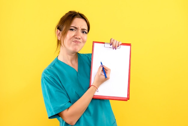Front view of female veterinarian holding pen and files on a yellow wall