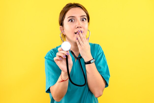 Front view of female veterinarian using stethoscope on a yellow wall