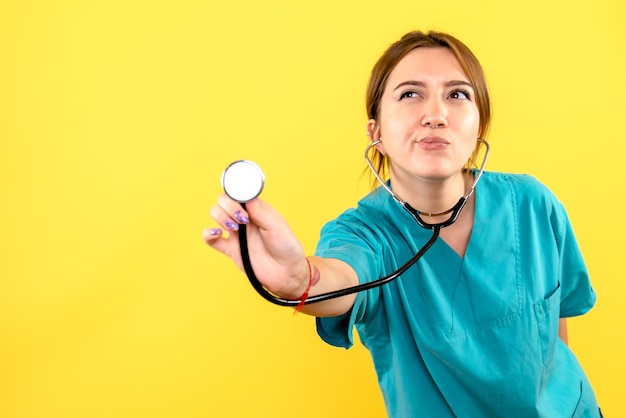 Front view of female veterinarian using stethoscope on yellow wall