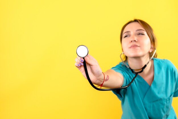 Front view of female veterinarian using stethoscope on yellow wall