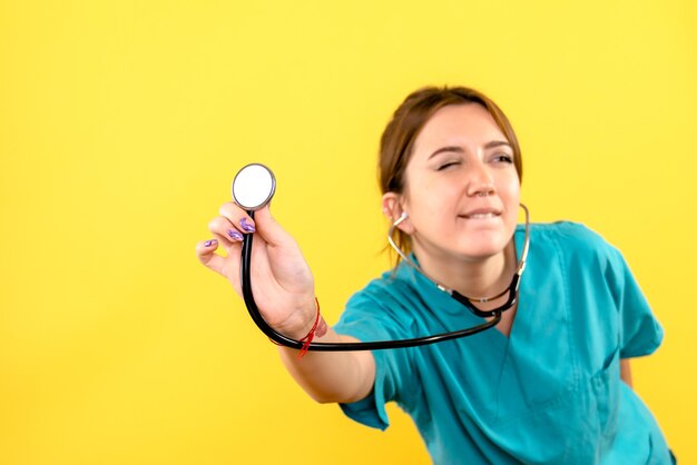Front view of female veterinarian using stethoscope on yellow wall