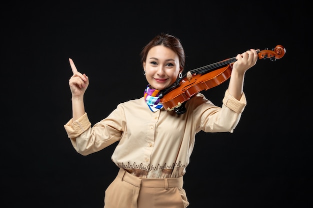 Free photo front view female violinist holding her violin on a dark wall woman concert melody emotion play instrument music