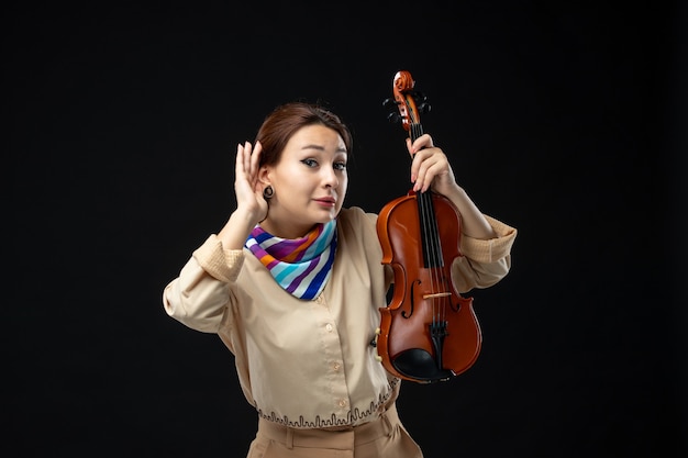 Front view female violinist holding her violin listening on dark wall
