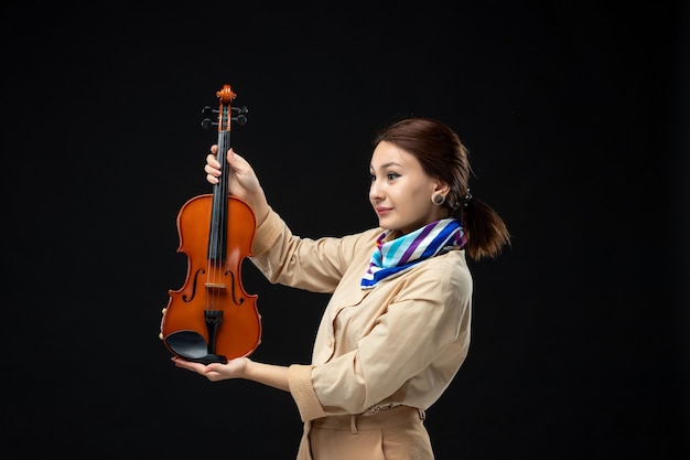 Foto gratuita vista frontale violinista femminile che tiene violino su parete scura melodia strumento donna performance musica emozione concerti concerti