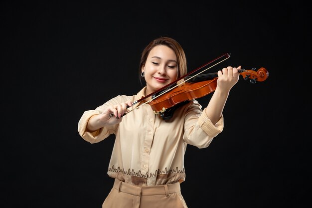 Front view female violinist playing on violin on dark wall music instrument play melody emotion woman