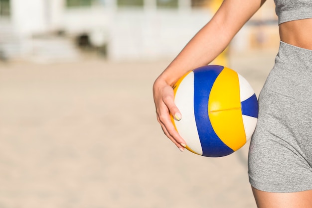 Front view of female volleyball player on the beach holding ball with copy space