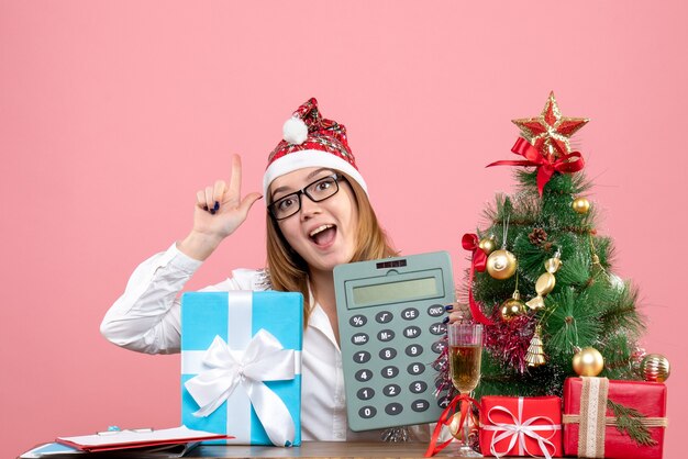 Вид спереди работницы, держащей калькулятор вокруг подарков на розовом