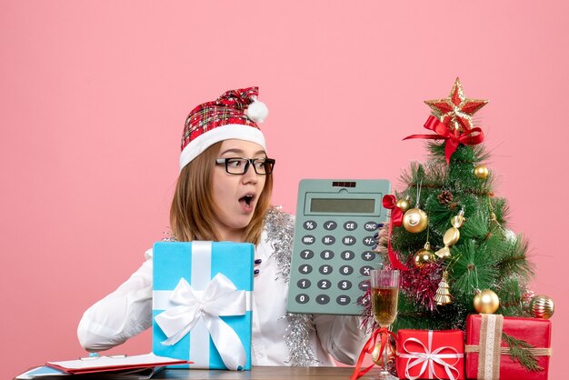 Front view of female worker holding calculator around presents on pink
