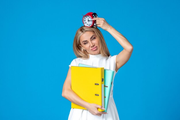 Front view of female worker holding folder and clock on blue wall