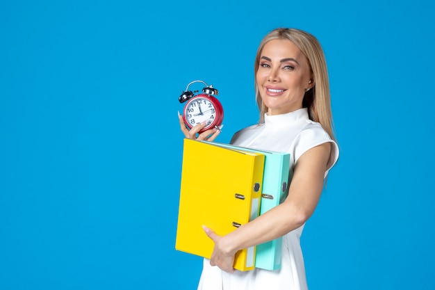 Front view of female worker holding folder and clock on blue wall
