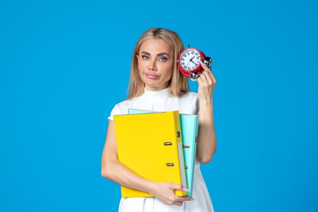 Front view of female worker holding folder and clock on blue wall