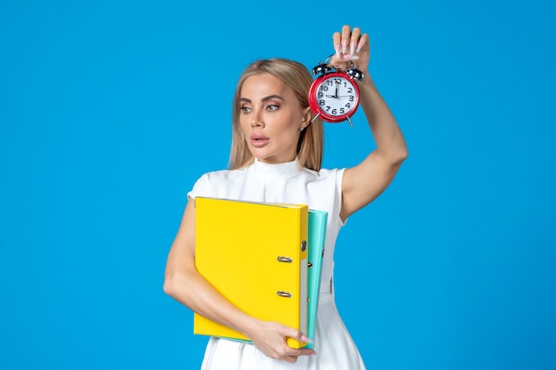 Front view of female worker holding folder and clock on blue wall