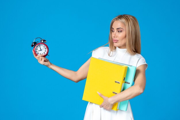 Front view of female worker holding folder and clock on blue wall