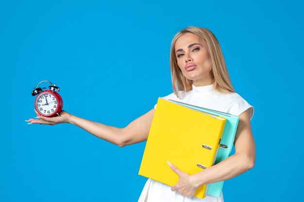 Front view of female worker holding folder and clock on blue wall