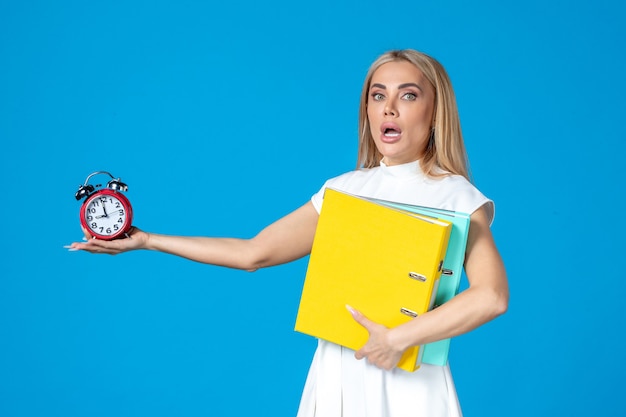 Front view of female worker holding folder and clock on blue wall