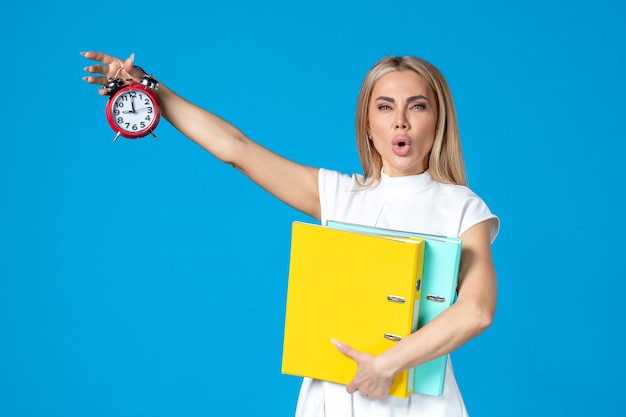 Front view of female worker holding folder and clock on blue wall