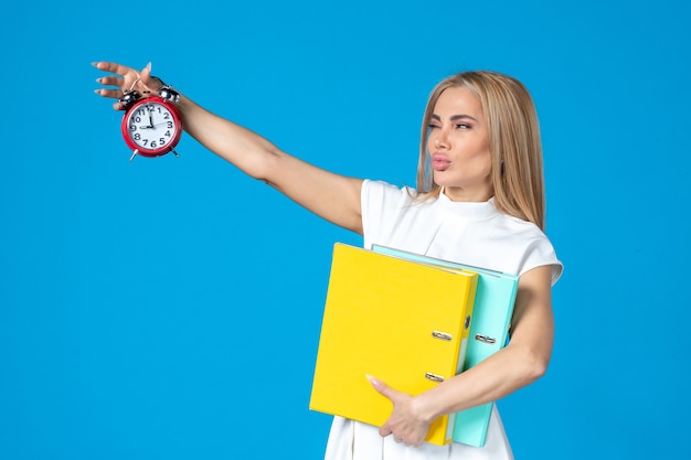 Front view of female worker holding folder and clock on blue wall