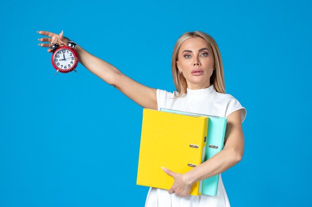 Front view of female worker holding folder and clock on blue wall