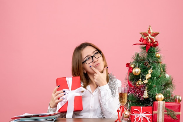 Front view of female worker holding present and thinking on pink