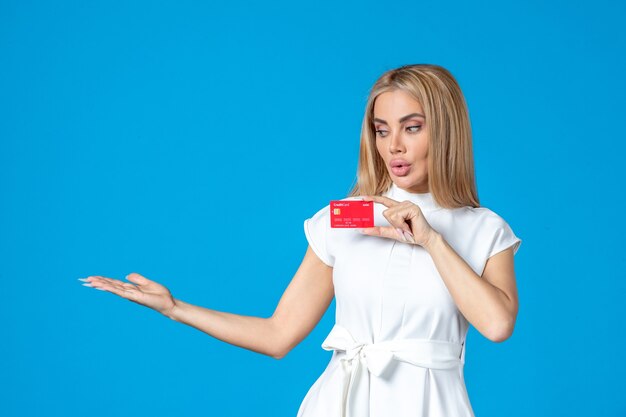 Front view of female worker holding red bank card on blue wall