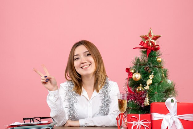 Front view of female worker sitting around christmas presents on pink