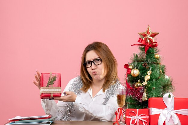 Front view of female worker sitting around christmas presents and tree on pink