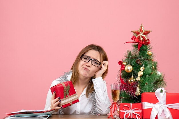 クリスマスプレゼントとピンクの木の周りに座っている女性労働者の正面図