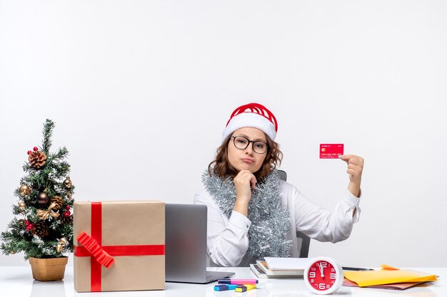 Вид спереди работница, сидящая перед своим рабочим местом, держащая банковскую карту, работа, бизнес, работа, рождественский офис, праздник