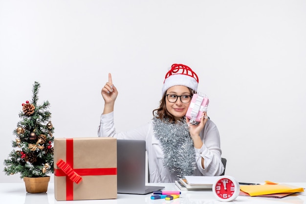 Vista frontale della lavoratrice seduta davanti al suo posto di lavoro con in mano una piccola lavoratrice presente lavoro d'ufficio di natale