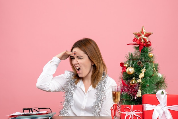 Front view of female worker sitting behind her table with christmas presents on pink