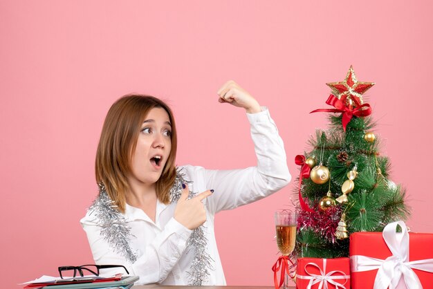 Front view of female worker sitting behind her table with christmas presents on pink