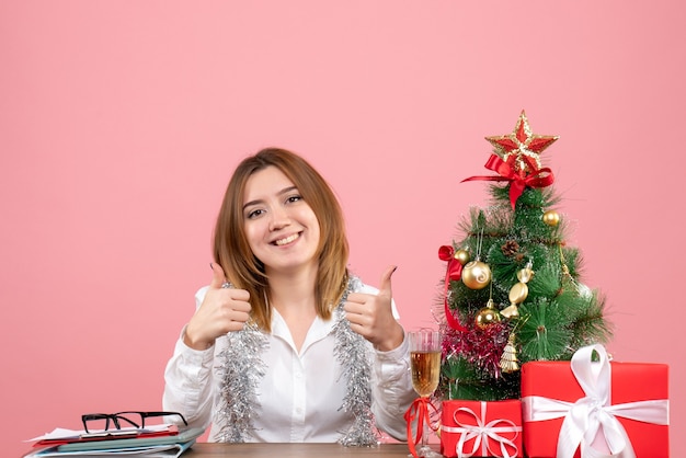 Вид спереди работницы, сидящей за своим столом с подарками, улыбаясь на розовом