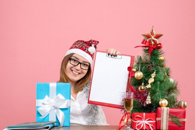 Front view of female worker sitting and holding file note around presents on pink