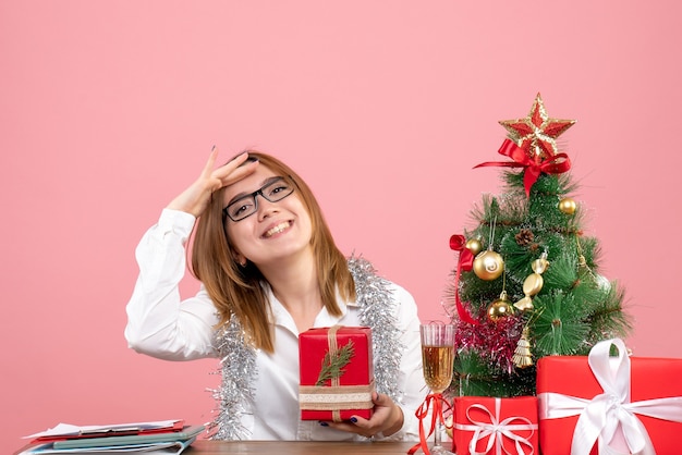 Front view of female worker sitting with christmas presents on pink