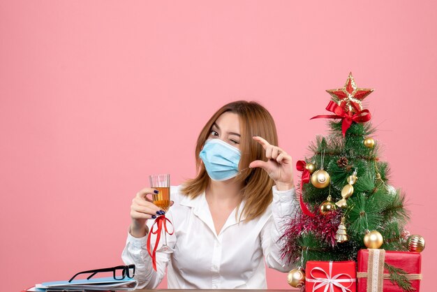 Front view of female worker in sterile mask celebrating xmas with champagne on pink