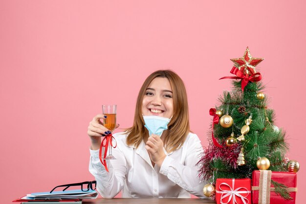 Front view of female worker in sterile mask celebrating xmas with champagne on pink