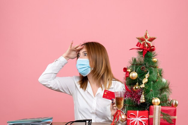 Front view of female worker in sterile mask holding bank card on pink