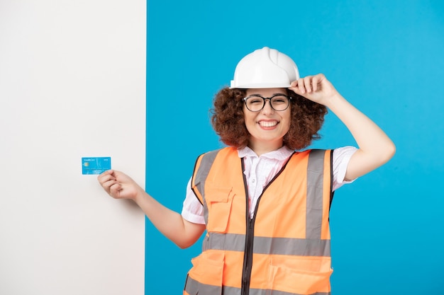 Front view of female worker in uniform with blue credit card on blue wall