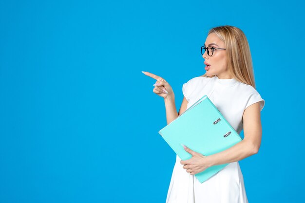 Front view of female worker in white dress holding blue folder on blue wall