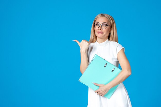 Front view of female worker in white dress holding blue folder on blue wall