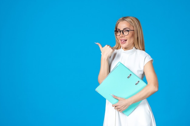 Front view of female worker in white dress holding blue folder on blue wall