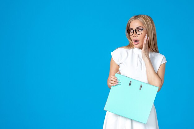 Front view of female worker in white dress holding blue folder on blue wall